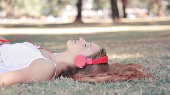 Junge Frau hört mit rotem Kopfhörer Musik in einem Park | Bildquelle: colourbox.com