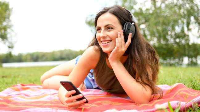 Eine Frau hört im Park über Kopfhörer Musik. | Bildquelle: picture alliance / dpa Themendienst | Tobias Hase