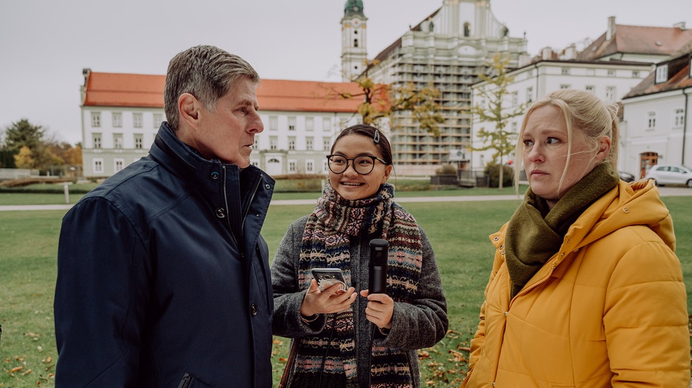 Dahoam is Dahoam: Vera (Sybille Waury, rechts) ist zunehmend genervt von Bambergers (Horst Kummeth) Besserwisserei. Mit Lien (Nui Nguyen). | Bildquelle: BR/Nadya Jakobs