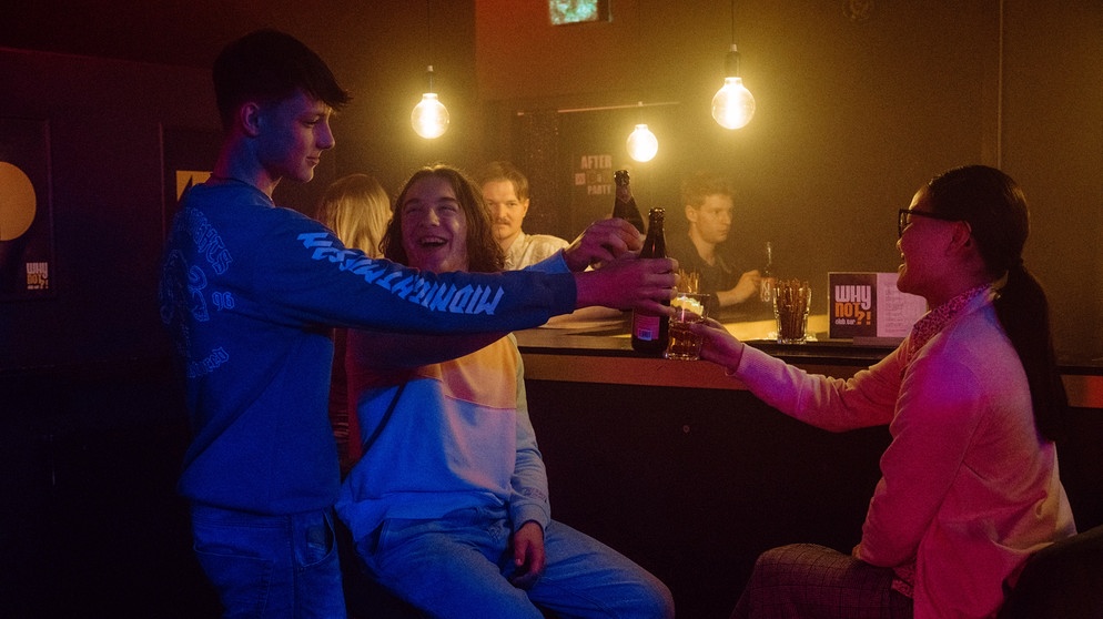 Dahoam is Dahoam: Hacki (Timo Baran, KLD, links), Till (Marinus Hohmann, Mitte) und Lien (Nui Nguyen, rechts) stoßen auf die bestandene Abschlussprüfung an. Mit Komparserie. | Bildquelle: BR/Nadya Jakobs