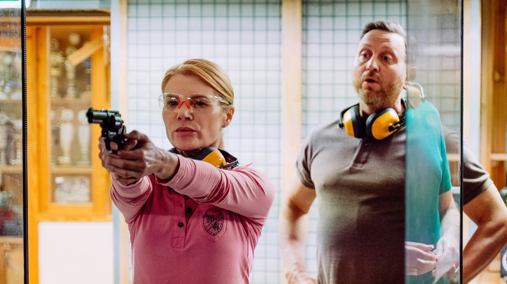 Dahoam is Dahoam: Uschi (Silke Popp) übt zum ersten Mal am Schießstand für ihren Waffenschein. Mit dem Schießlehrer (Stefan Pfau). | Bildquelle: BR/Nadya Jakobs