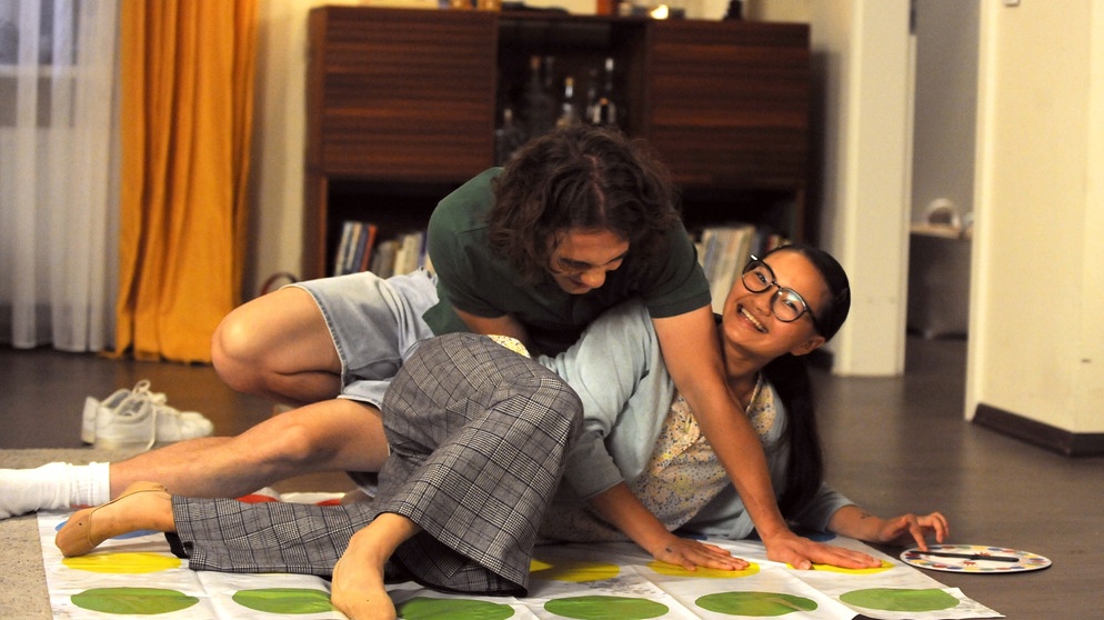 Dahoam is Dahoam: Lien (Nui Nguyen) und Till (Marinus Hohmann) spielen in der WG gemeinsam Twister. | Bildquelle: BR/Marco Orlando Pichler