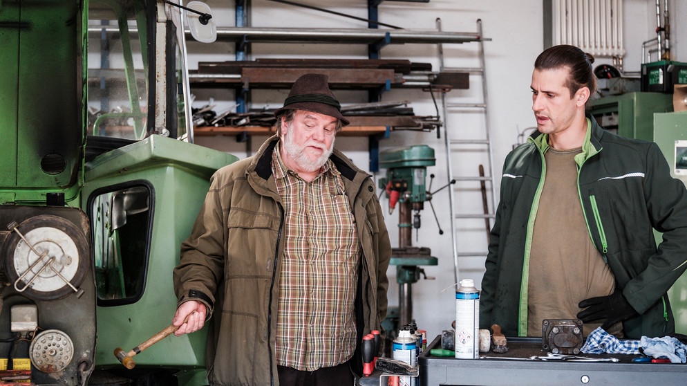 Dahoam is Dahoam: Julian (Sandro Kirtzel, rechts) muss Stadlbauer (Andreas Geiss, links) erklären, wieso der Traktor nicht funkioniert. | Bildquelle: BR/Lena Semmelroggen