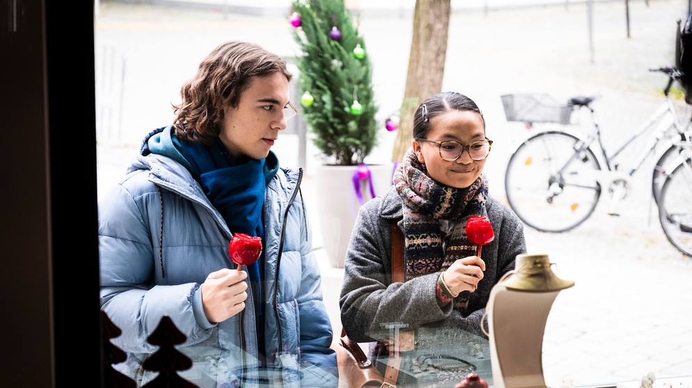 Dahoam is Dahoam: Lien (Nui Nguyen) steht mit Till (Marinus Hohmann) vor einem Schaufenster und versucht subtil ihm einen Tipp zu geben, was ihr gefällt. | Bildquelle: BR/Lena Semmelroggen