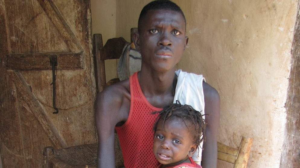 alpha-demokratie weltweit - Leben mit dem Handicap / Junger duenner, durch Polio behinderter Mann mit kleinem Kind auf dem Schoss in laendlicher Gegend ohne guten Zugang zu medizinischer Versorgung, Haiti, Grande Anse, Jeremie | Bildquelle: picture-alliance/dpa