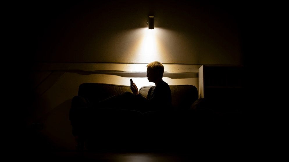 alpha-thema Gespräch: Psyche, Stress und Pandemie | Symbolbild zum Thema Einsamkeit und Isolation: Eine Frau sitzt nachts auf der Couch und schaut in ein Smartphone. | Bildquelle: picture alliance / photothek | photothek/ Thomas Trutschel