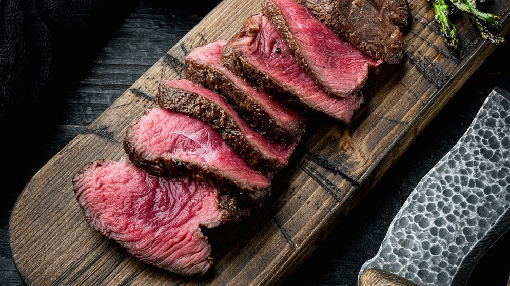 Aufgeschnittenes und gegrilltes Rinderfilet, mit Zwiebeln und Spargel auf einem hölzernen Servierbrett angerichtet. | Bildquelle: stock.adobe.com/Ilia Nesolenyi