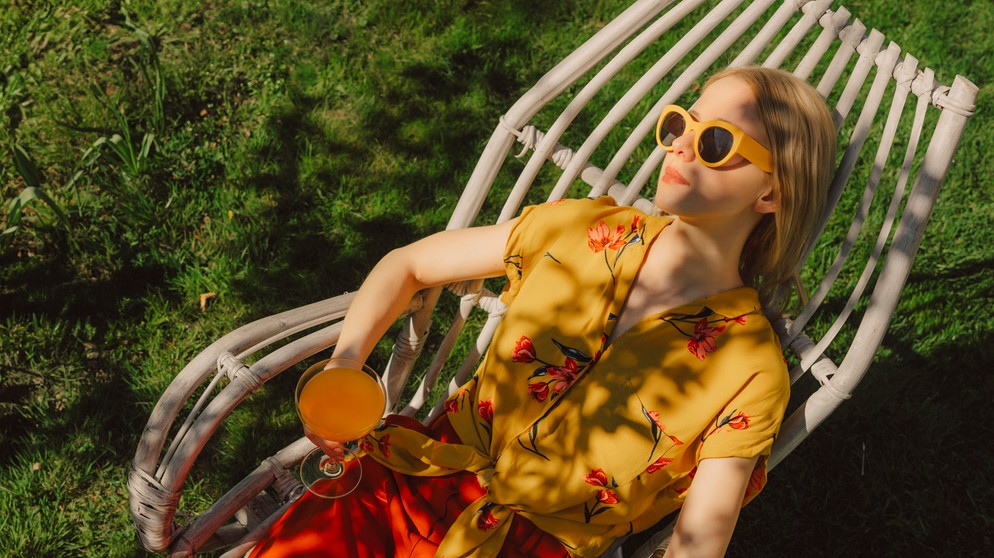 Frau liegt in einem Gartenstuhl mit Cocktail in der Hand | Bildquelle: picture alliance / Westend61 | Vira Simon