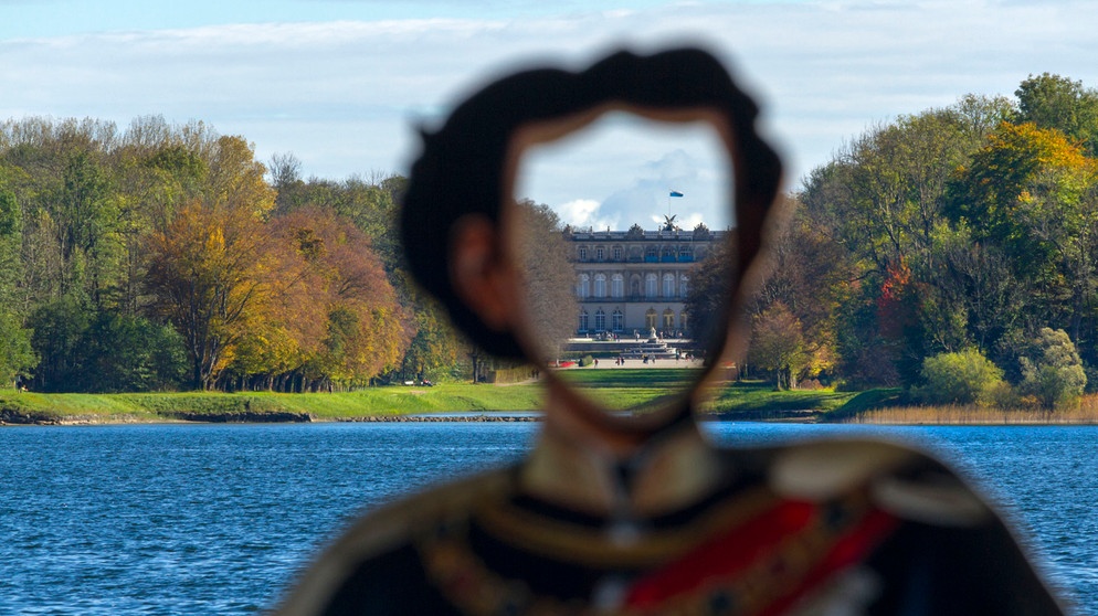 Blick auf Schloss Herrenchiemsee, davor die Umrisse einer König Ludwig II. Skulptur. | Bildquelle: picture alliance / Paul Mayall | Paul Mayall