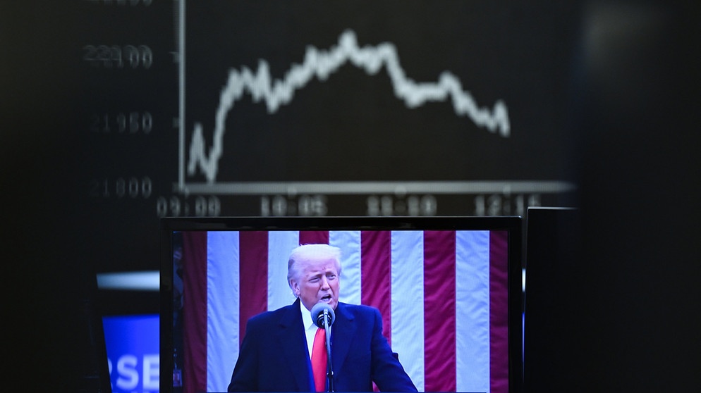 03.04.2025, Hessen, Frankfurt/Main: Hinter einem Fernsehmonitor, auf dem US-Präsident Donald Trump zu sehen ist, zeigt die Anzeigetafel mit der Dax-Kurve fallende Kurse. (zu dpa: «US-Zollpaket treibt Anleger in die Flucht») Foto: Arne Dedert/dpa +++ dpa-Bildfunk +++ | Bildquelle: dpa-Bildfunk/Arne Dedert