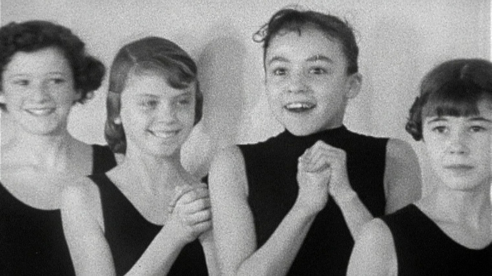 Gezeigt wird in diesem Film von 1958 ein Tag in den Trainingsräumen des Balletts der Bayerischen Staatsoper, die damals noch nicht restauriert war und unverhüllt die Bombenschäden aus dem Zweiten Weltkrieg zeigte. Zuerst trainieren die Erwachsenen, danach die Kleinen, also die Kinder von ungefähr 7 Jahren an. Zu diesen jungen Mädchen kommt dann der Ballettmeister, er sucht für ein neues Stück Tänzerinnen, die auf der Bühne kleine Tauben darstellen sollen. Große Aufregung: Wer darf mitmachen? | Bildquelle: BR