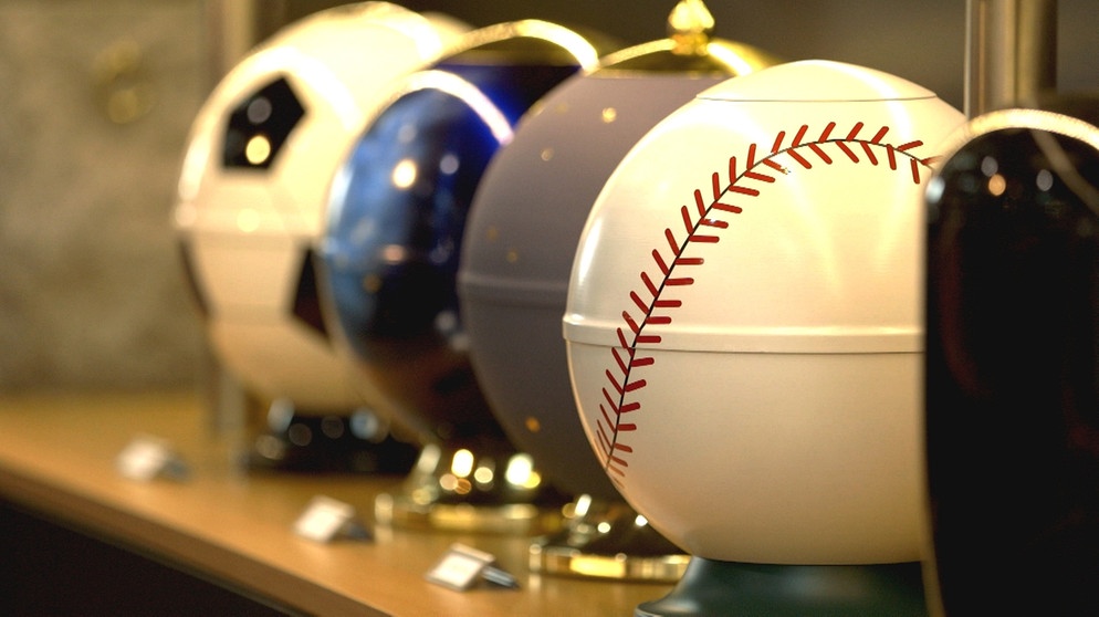 Moderne Urnen in Form von Sportbällen, etwa Fußball oder Baseball, auf der Internationalen Bestattungsfachausstellung (BEFA) 2018 in Düsseldorf. | Bildquelle: BR