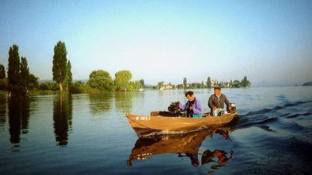 SWR-Kameramann im Boot eines Bodenseefischers. Im Hintergrund die Insel Reichenau. | Bildquelle: BR/SWR