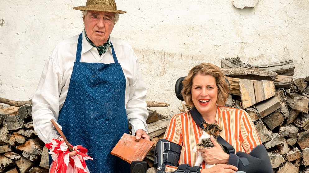 Key Visual - Nach einem missglückten Reparatureinsatz und einem Sturz, kann sich Hofbesitzerin Sophie (Elena Uhlig) nun wochenlang nur im Rollstuhl fortbewegen. Um ihre Gäste zu versorgen, springt Stallbewohner Barthl (Friedrich von Thun) notgedrungen in die Bresche. | Bildquelle: ARD Degeto/Marc Reimann