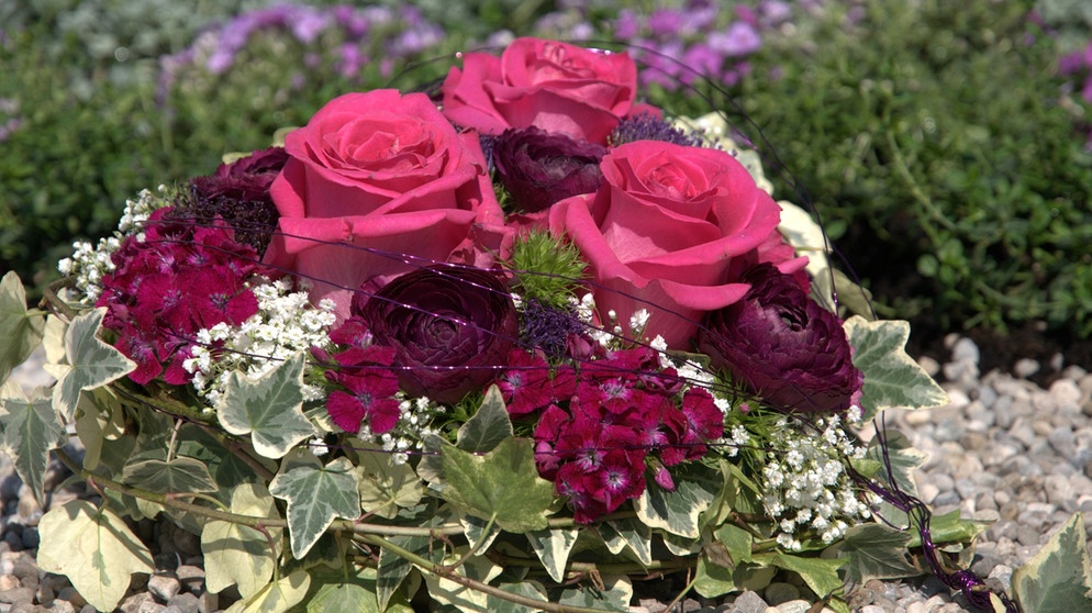 Rosarotes Blumengesteck mit Rosen, Ranunkeln, Bartnelken und Efeu auf einem Grab. | Bildquelle: BR
