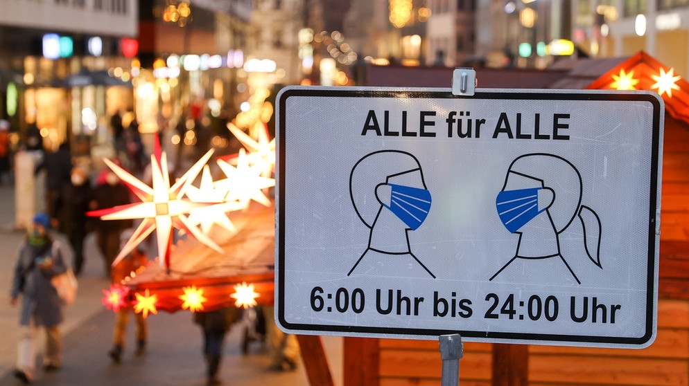 Schild mit der Aufschrift "Alle für Alle - 6:00 bis 24:00 Uhr", das auf die Maskenpflicht hinweist, vor Fußgängerzone mit Weihnachts-Deko | Bildquelle: dpa-Bildfunk/Jan Woitas