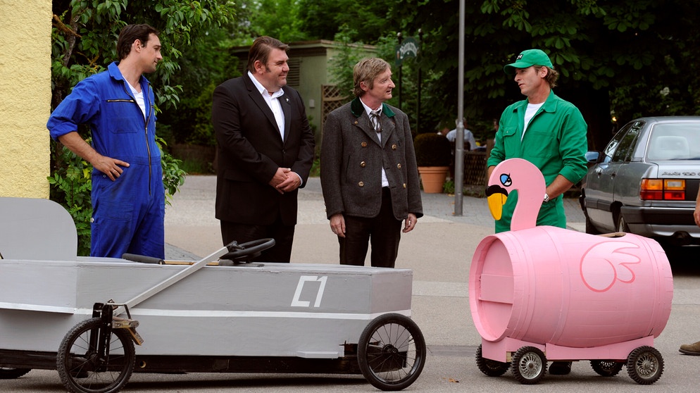 Mike und Sebastian wollen sich gegenseitig mit ihren selbst gebauten Seifenkisten übertrumpfen. Von links: Mike Preissinger (Harry Blank), Pfarrer Neuner (Peter Rappenglück), Xaver (Michael Schreiner) und Sebastian Wildner (Herbert Ulrich). | Bildquelle: BR/Marco Orlando Pichler