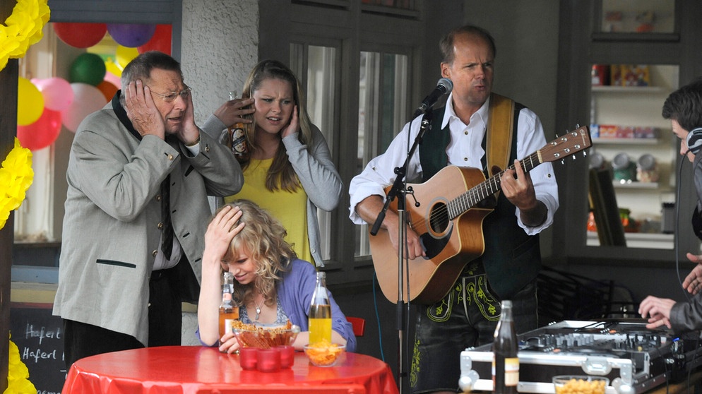 Die Eröffnungsfeier von Kiosk und Jugendtreff verläuft äußerst skurril. Von links: Alois Preissinger (Erich Hallhuber sen.), Caro Ertl (Teresa Rizos), Yvonne Preissinger (Alexa Eilers) und ein Schlagersänger (Andreas Lipperer). | Bildquelle: BR/Marco Orlando Pichler
