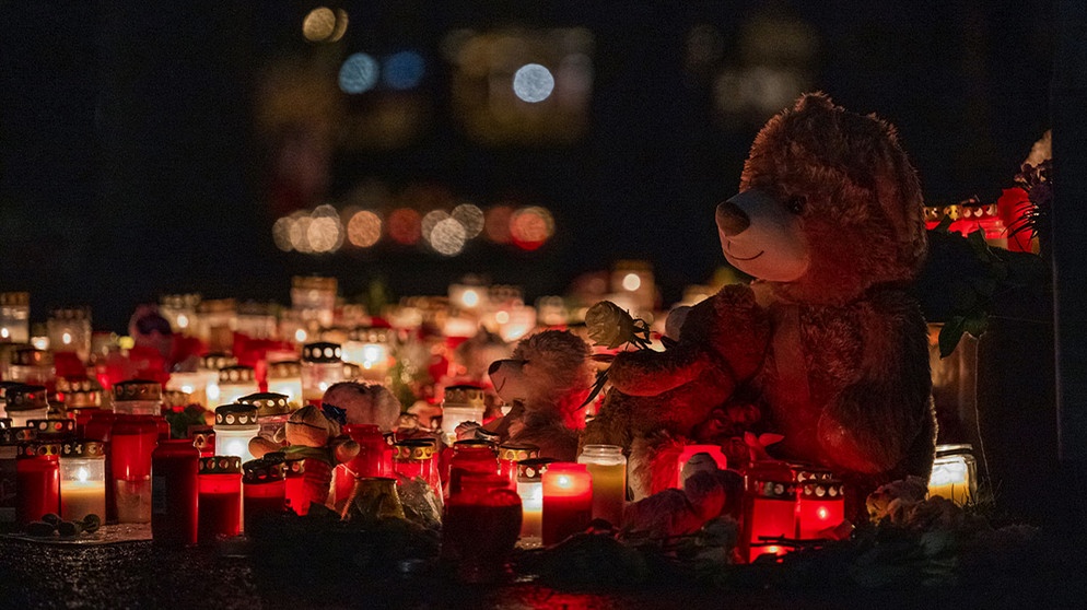 Ein Teddybär steht zusammen mit zahlreichen Kerzen auf dem Boden und erinnert an den tödlichen Messerangriff. Zahlreiche Kerzen und Kuscheltiere erinnern am Freitagmorgen im Park Schöntal an die Opfer der tödlichen Messerattacke. | Bildquelle: picture alliance/dpa | Daniel Vogl