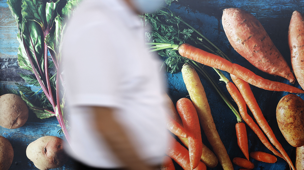 Symbolbild für Campus talks: Passanten laufen an einer Außenwerbung an einem REWE-Markt in Köln vorbei, die frisches Gemüse zeigt.  | Bildquelle: picture alliance / Geisler-Fotopress | Christoph Hardt/Geisler-Fotopres