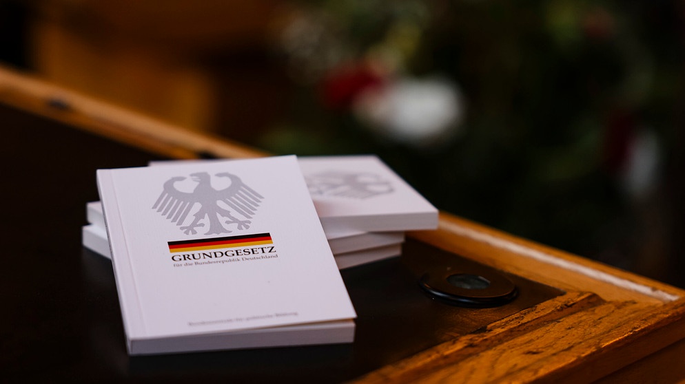 Vier Bücher mit dem Grundgesetz liegen während einer Einbürgerungsfeier auf einem Tisch im Ratssaal des Kieler Rathauses. In der Landeshauptstadt wurden im Jahr 2022 781 Personen eingebürgert. | Bildquelle: dpa-Bildfunk/Frank Molter