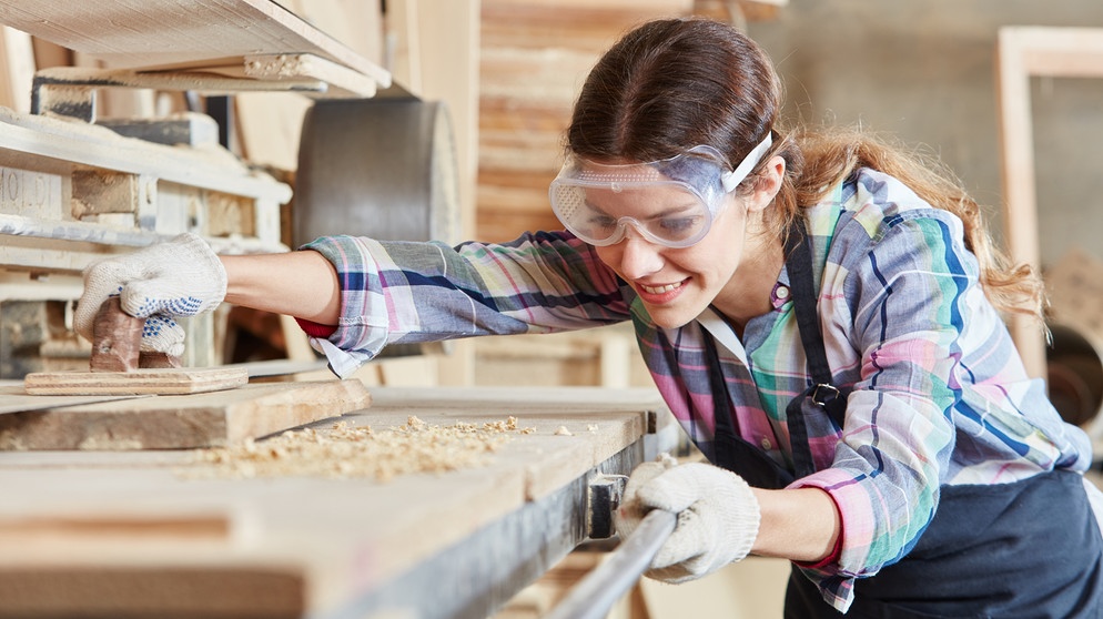 Frau als Tischler schleift Holz am Bandschleifer in der Tischlerei. | Bildquelle: stock.adobe.com/Robert Kneschke