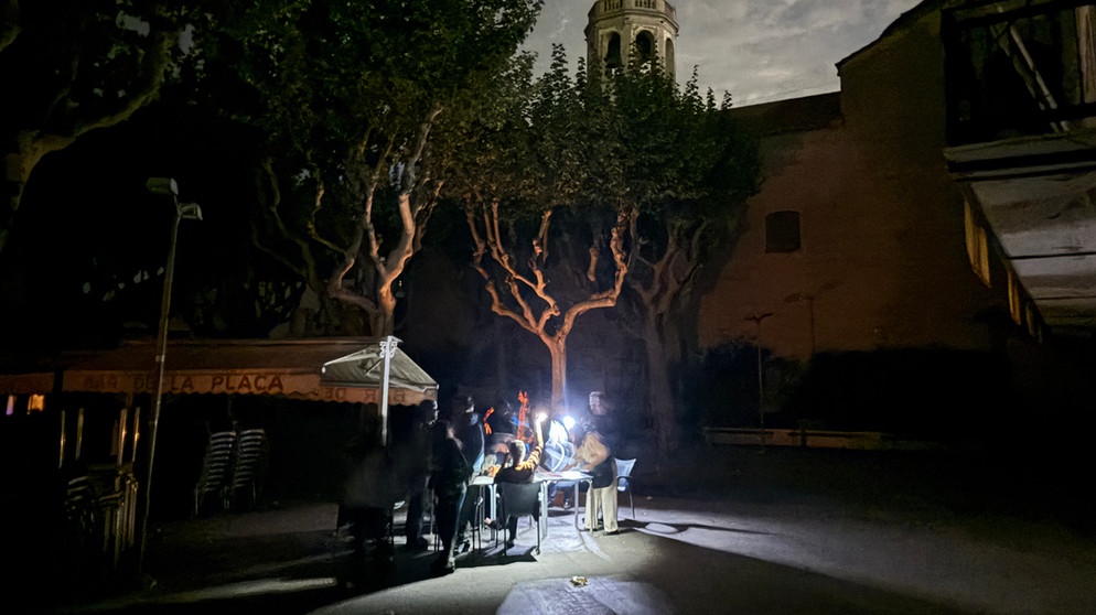 dpatopbilder - 28.04.2025, Spanien, Premià de Mar: Auf der Placa de l'Ajuntament sitzen die Gäste eines Straßencafés in der Kleinstadt Premià de Mar bei Barcelona an der Kirche "San Cristòfol" bei einem Stromausfall im Licht von Taschenlampen und trinken lauwarmes Bier. Nach dem großflächigen Blackout vom Montag haben fast alle Menschen in Spanien und Portugal inzwischen wieder Strom. Der spanische Versorger Red Eléctrica teilte am frühen Dienstagmorgen mit, über 99 Prozent der Energieversorgung seien auf dem vom Ausfall betroffenen Festland wiederhergestellt worden. Foto: Jan-Uwe Ronneburger/dpa +++ dpa-Bildfunk +++ | Bildquelle: dpa-Bildfunk/Jan-Uwe Ronneburger
