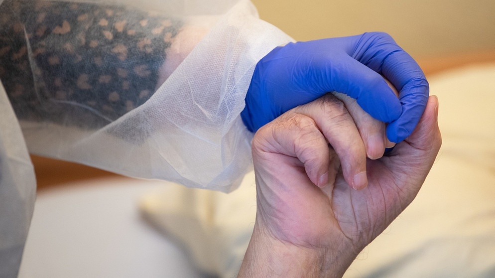 Tübingen: Eine Altenpflegerin in Schutzkleidung hält die Hand eines Bewohners.  | Bildquelle: Sebastian Gollnow/dpa