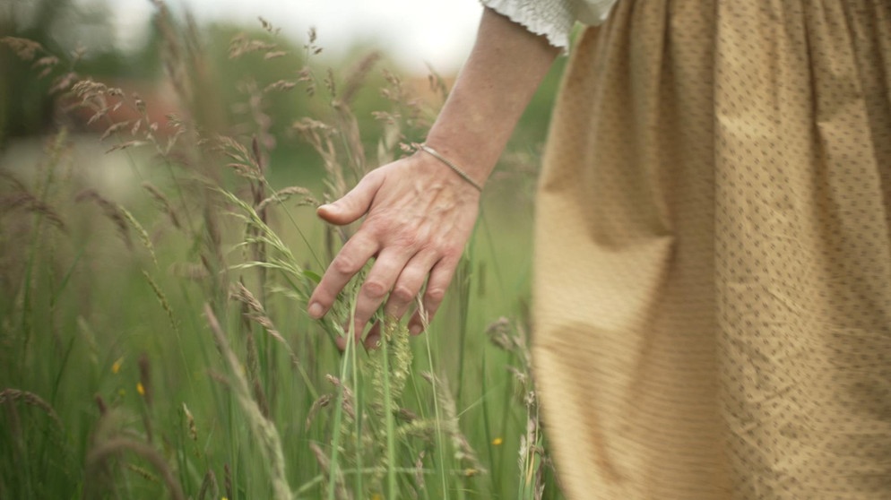 Eine Frau streift mit der Hand durch eine Wiese | Bildquelle: BR 