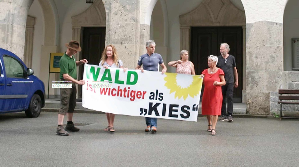 Foto einer Bürgerinitiative mit einem Plakat in der Hand mit der Aufschrift: Wald ist wichtiger als Kies. | Bildquelle: BR