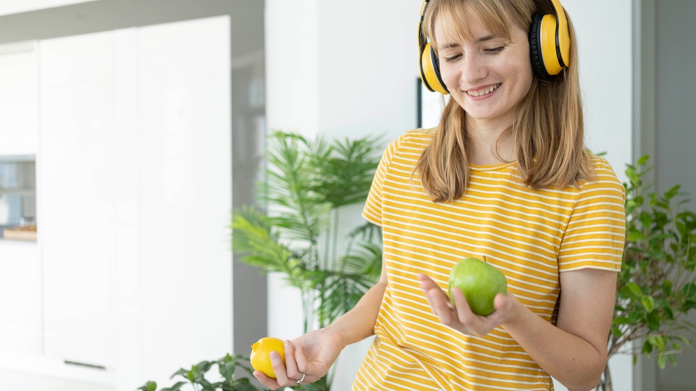 Happy woman wearing wireless headphones holding green apple and lemon | Bildquelle: picture alliance / Westend61 | Svetlana Karner