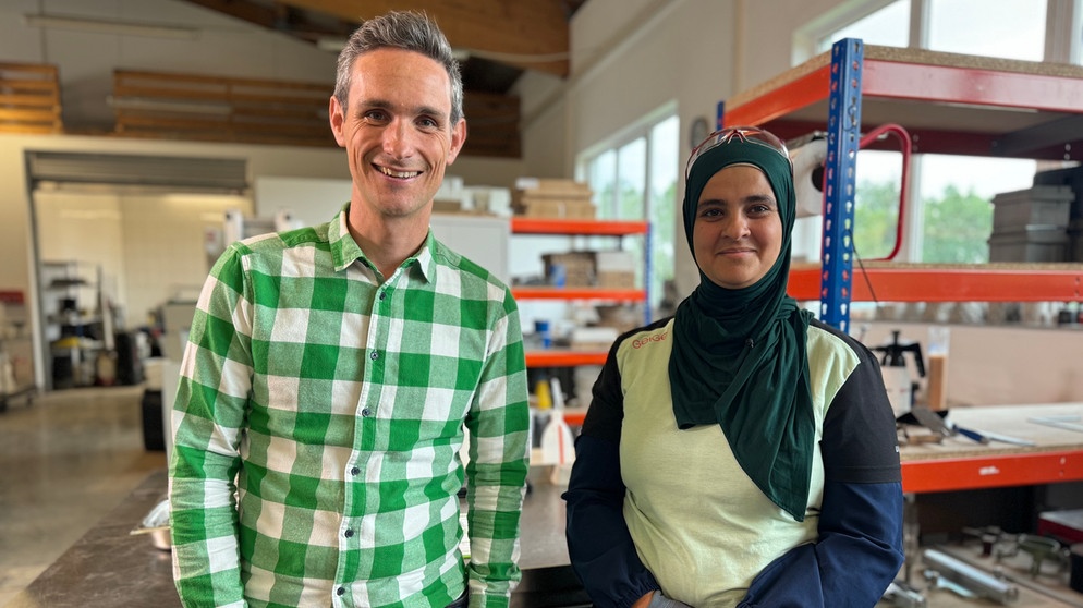 STATIONEN-Moderator Benedikt Schregle mit Amina Marwa an ihrem Arbeitsplatz. | Bildquelle: BR