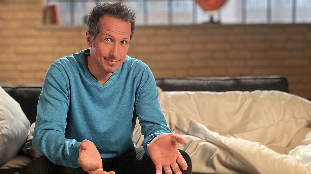 "Gut zu wissen"-Moderator Willi Weitzel sitzt auf einer Couch mit Bettdecke. In der Sendung beschäftigt er sich mit dem Thema "besser schlafen". | Bildquelle: BR/Gut zu wissen 