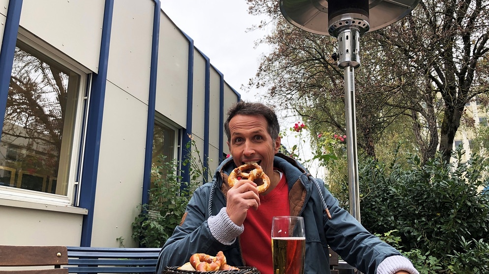 "Gut zu wissen"-Moderator Willi Weitzel sitze im Freien beim Brotzeit machen, mit einem Heizpilz im Hintergrund.  | Bildquelle: BR/Gut zu wissen