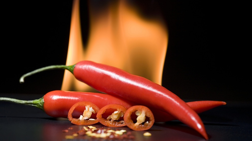 Scharfe Chilis mit Feuer im Hintergrund. Die Schärfe löst einen "Pepper-high" im Mund aus und kann süchtig machen. | Bildquelle: picture-alliance/dpa