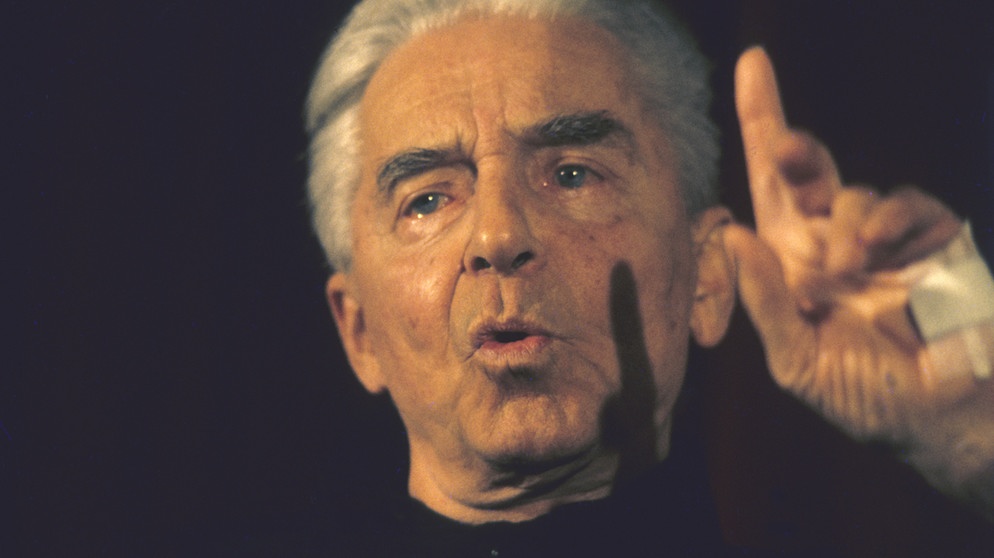 Herbert von Karajan: Der Dirigent streckt seinen Zeigefinger bei einer Pressekonferenz | Bildquelle: picture-alliance/dpa